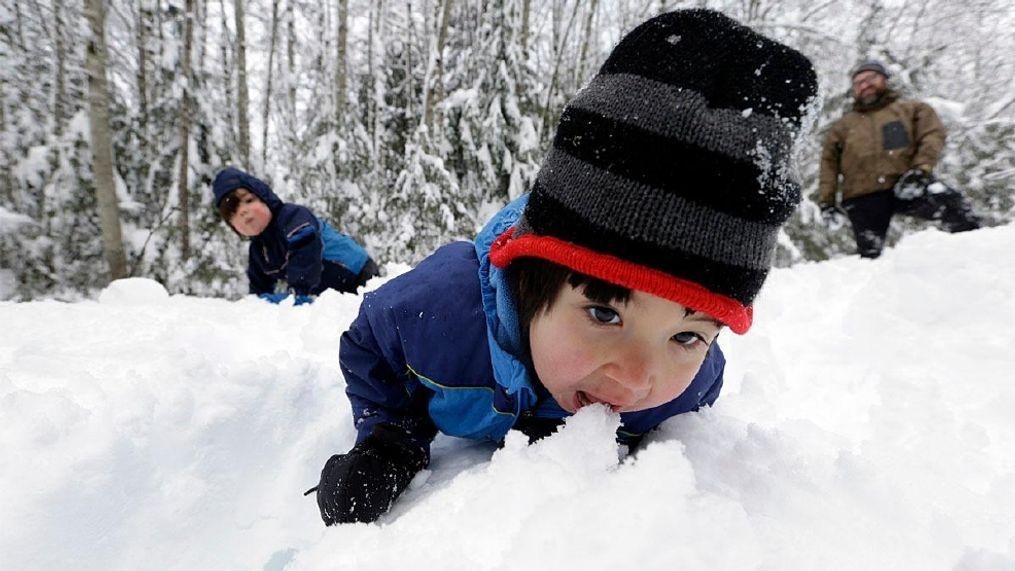 Leon Perkins, 3, leans forward to take a bite of snow as he plays with his brother Conner, left, 2, and his father Erin, Tuesday, Dec. 22, 2015, at Snoqualmie Pass, Wash.  (AP Photo/Elaine Thompson)