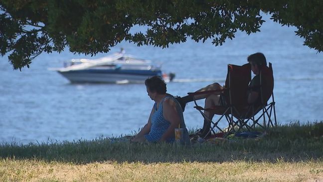 FILE – Two people sit in the shade underneath a tree by the water to escape the heat. (KOMO News)